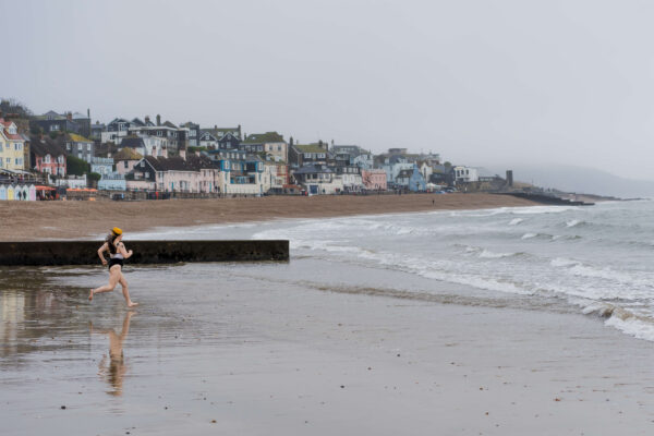 Mil running along a beach in the shallows with a coastal town visible in the background